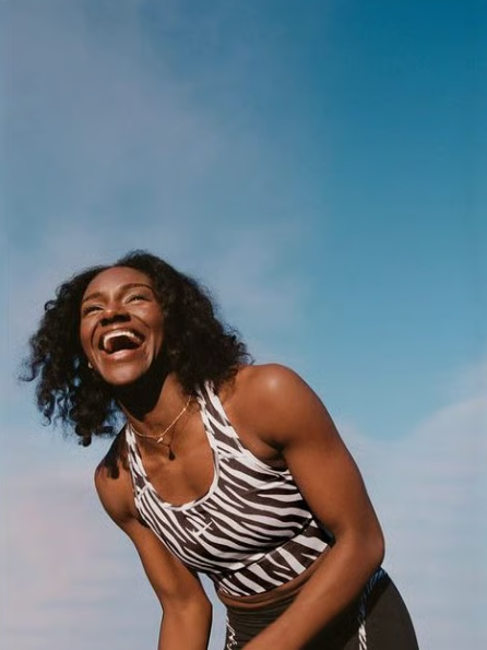 Laughing woman in a zebra-striped sports top reaching toward the camera against a clear blue sky